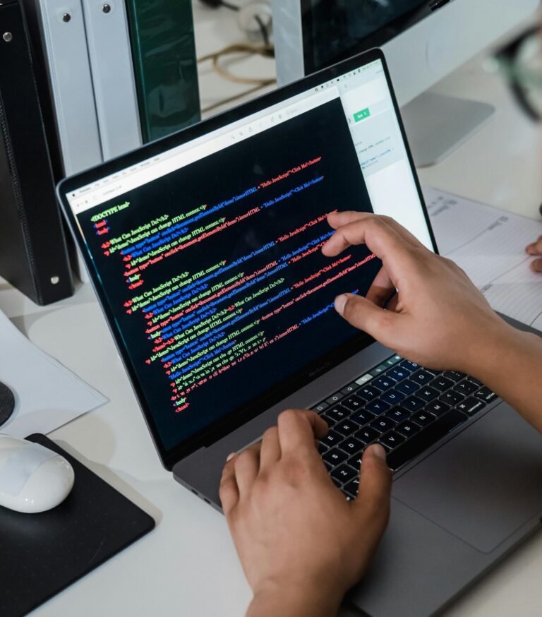 Close-up of a programmer pointing at a colorful code script on a laptop in an office setting.