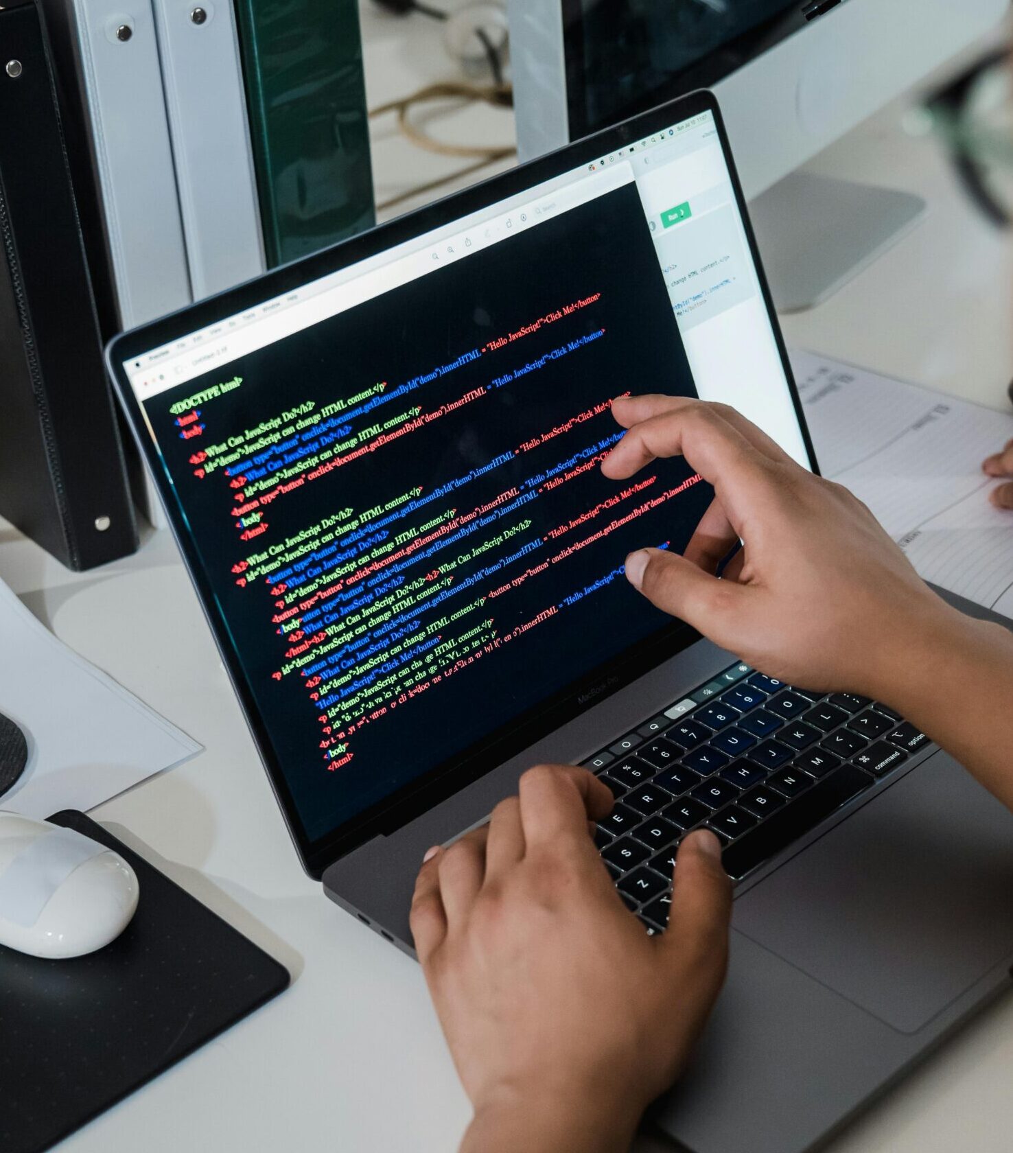 Close-up of a programmer pointing at a colorful code script on a laptop in an office setting.
